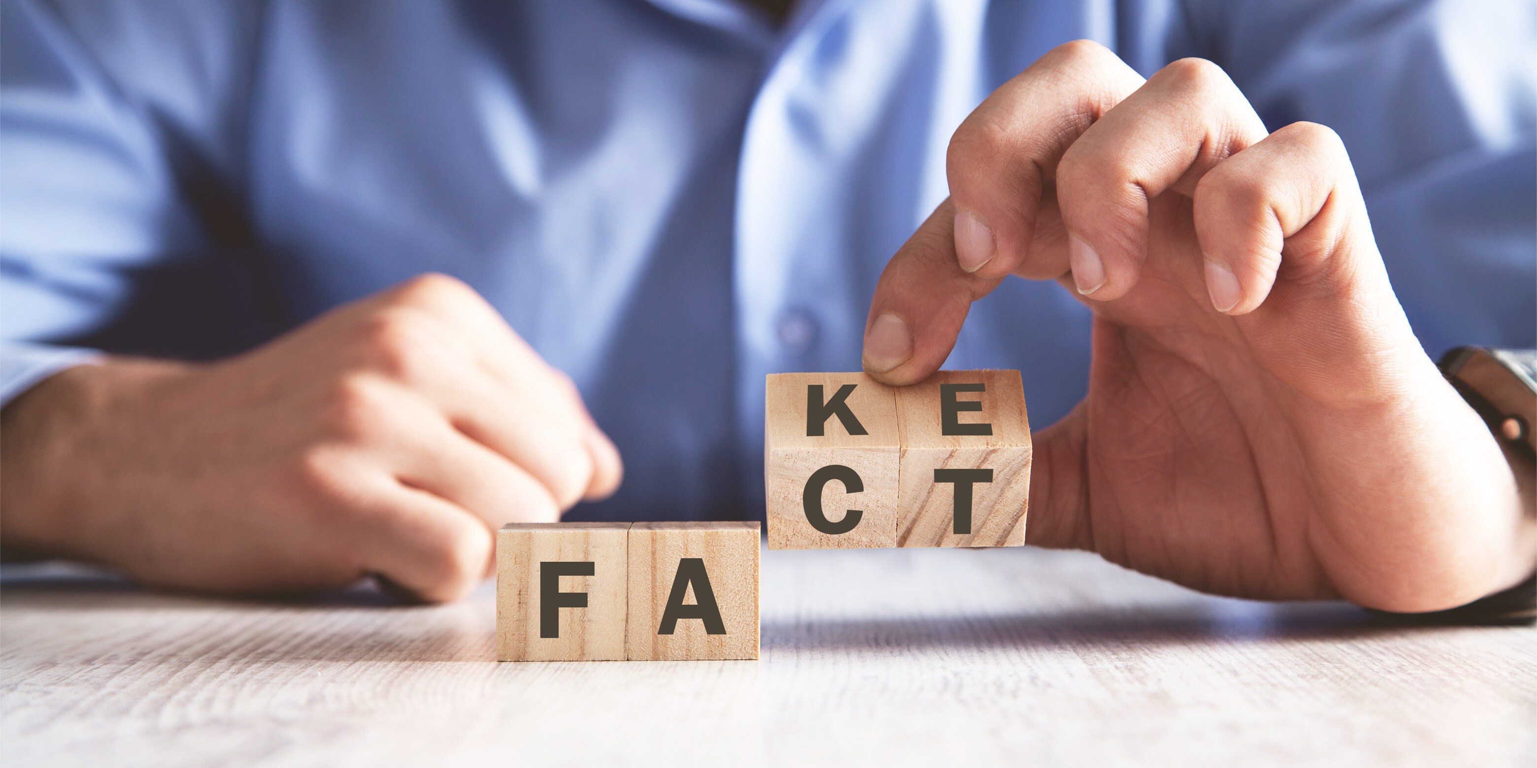 Photo of hands rotating block that change a word from fact to fake.