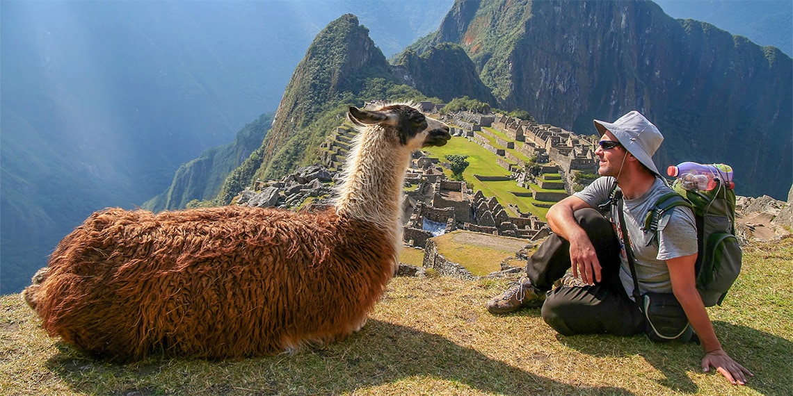 Image of man sitting next to a llama in Machu Picchu.